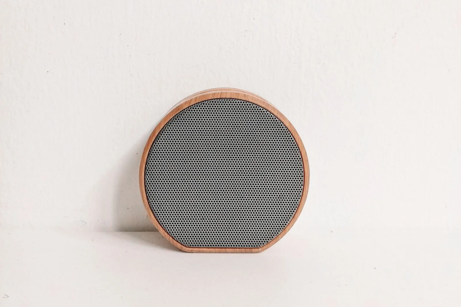 A round wireless speaker against a white wall