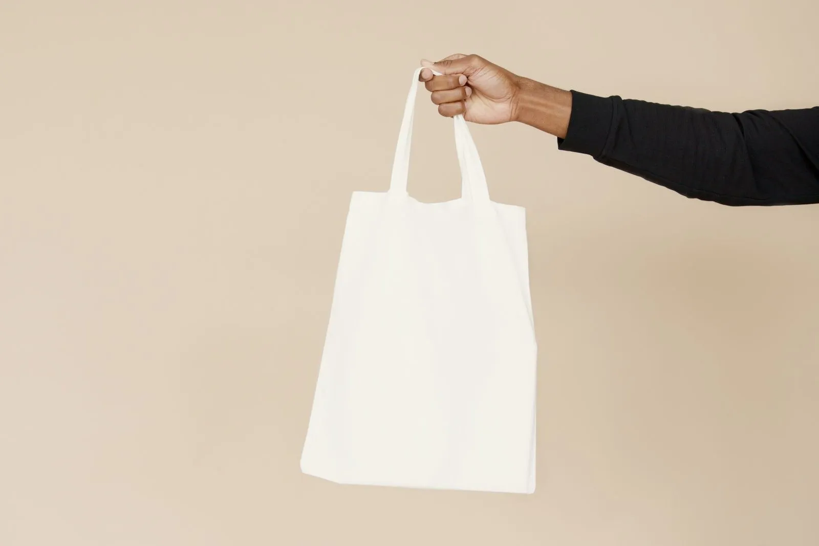 A plain canvas tote bag held against a beige wall