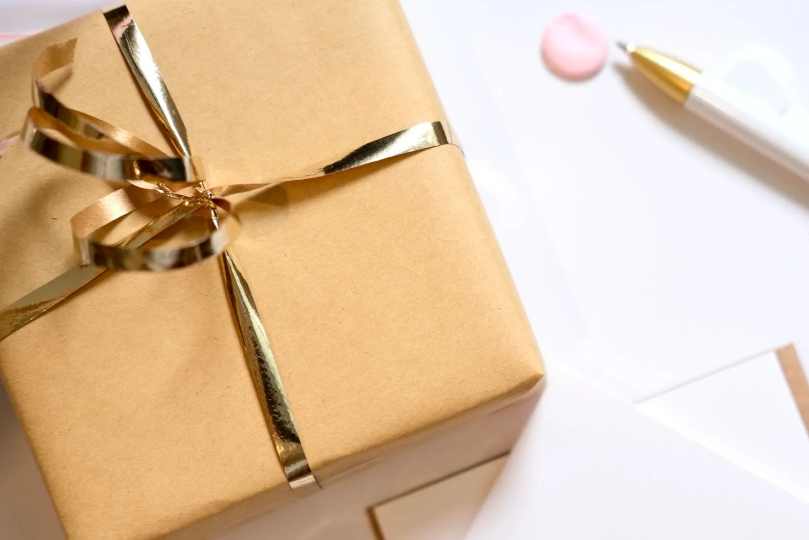 A kraft gift box tied with gold ribbon beside a pen and a blank card